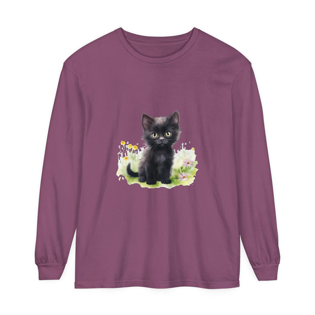 A cute black kitten sitting in a colorful flower garden on a long sleeve t-shirt