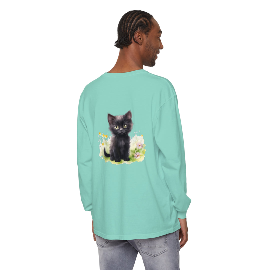 A cute black kitten sits amidst a vibrant flower garden on a long sleeve t-shirt