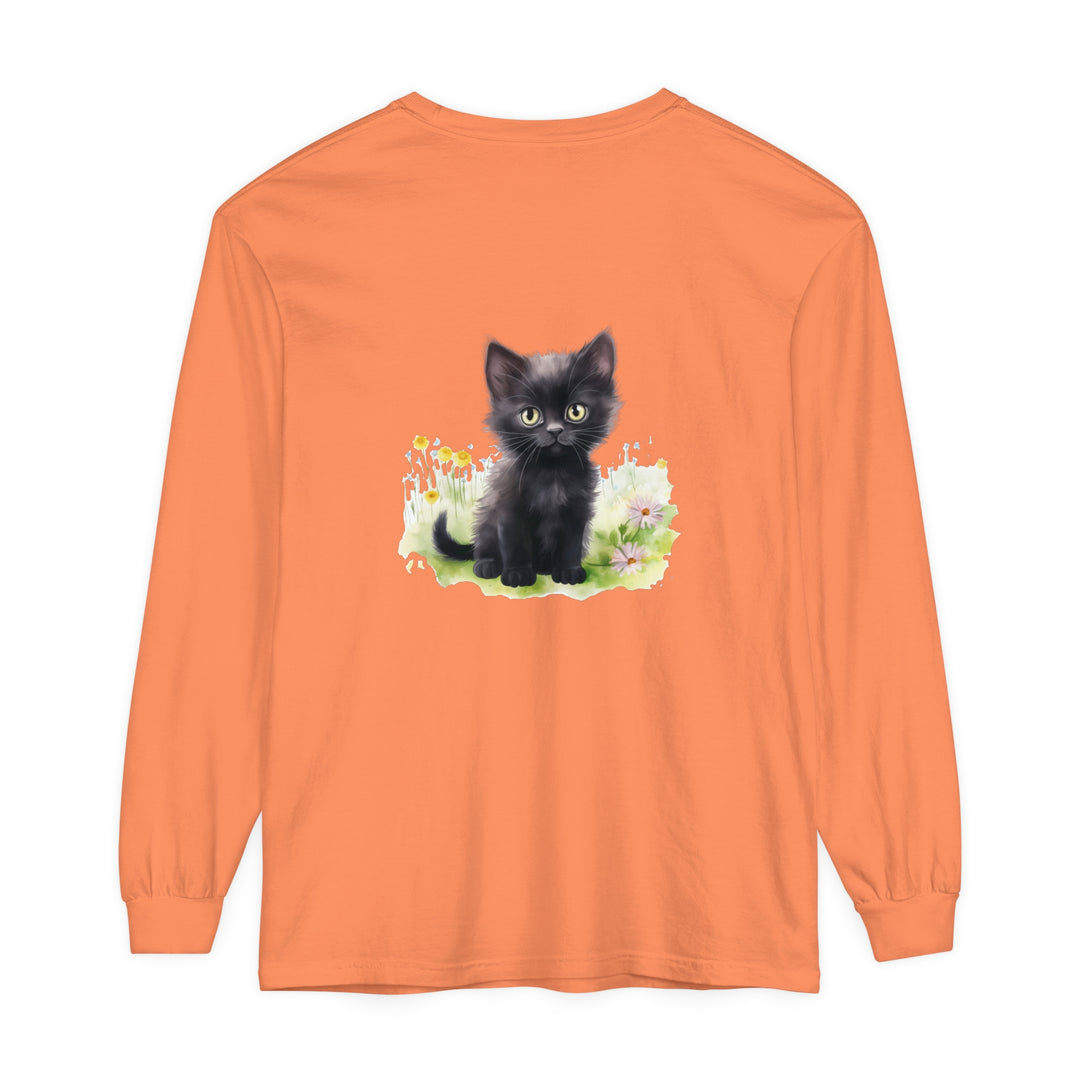 A cute black kitten sits among colorful flowers in a garden on a long sleeve t-shirt