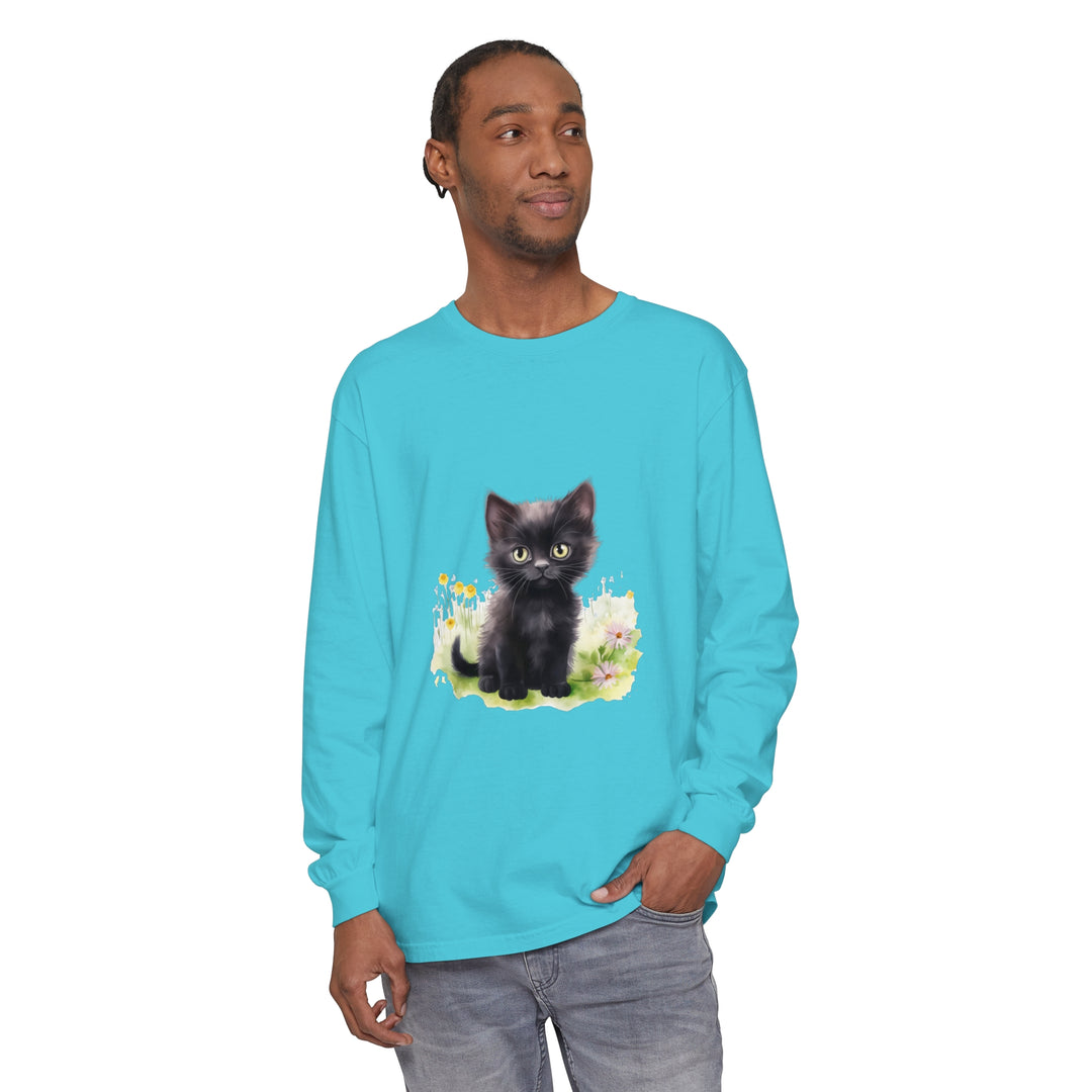 A cute black kitten sits in a vibrant flower garden on a long sleeve t-shirt