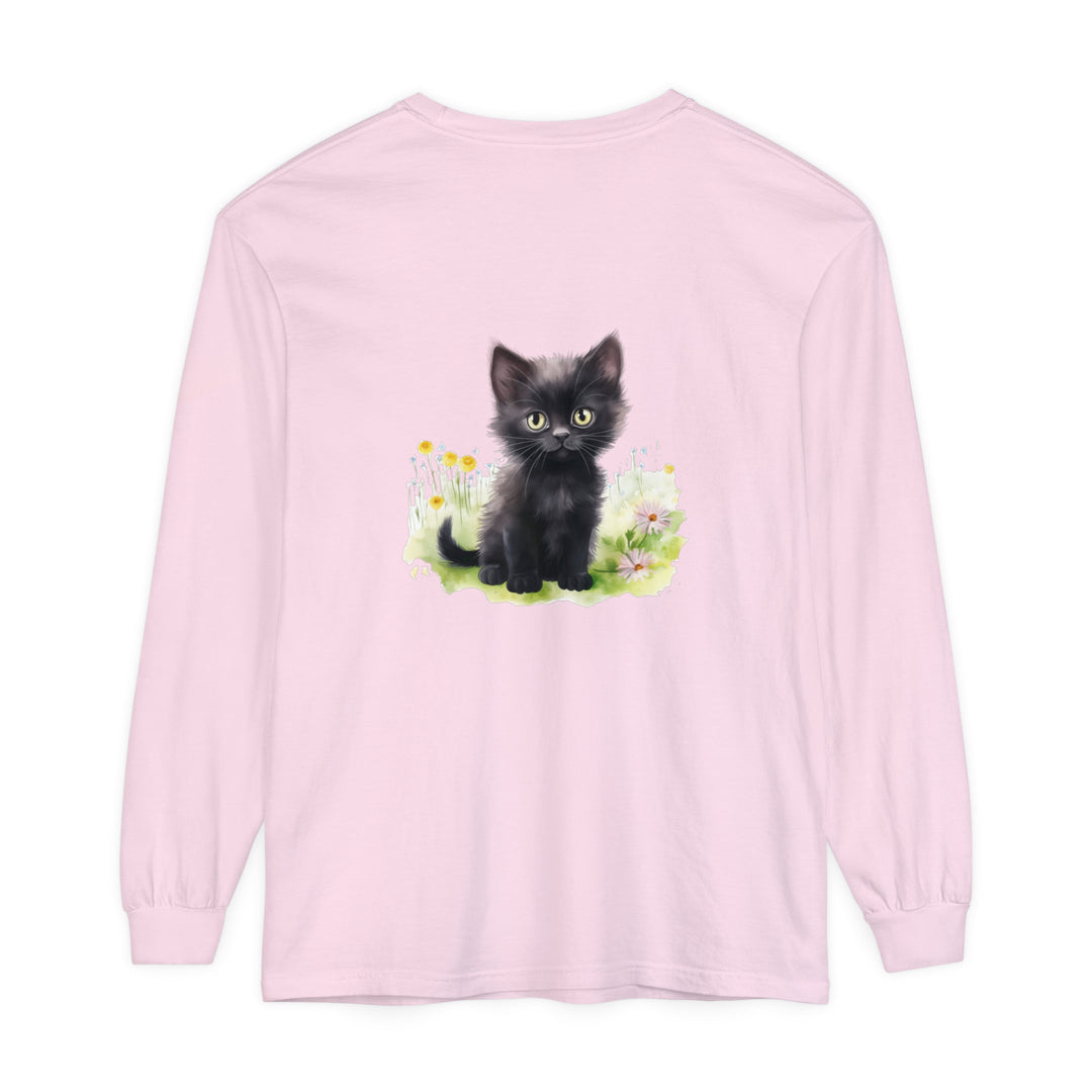 A cute black kitten stands in a vibrant flower garden on a long sleeve t-shirt