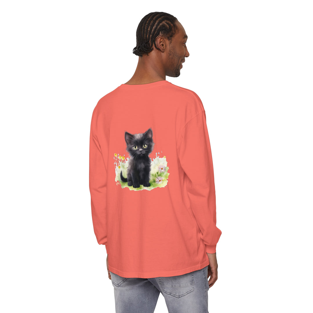 A cute black kitten sits in a colorful flower garden on a long sleeve t-shirt