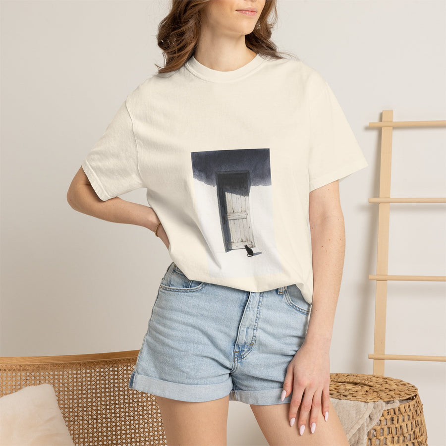 A woman wearing a cream-colored oversized graphic t-shirt with a black and white art print of a door, paired with light-wash denim shorts, in a brightly lit indoor setting.