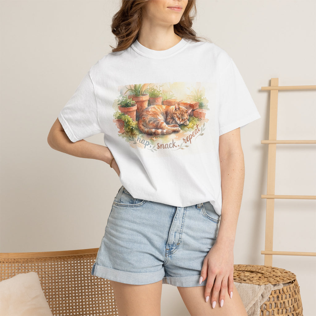 Person wearing a white t-shirt with a cat graphic and text, standing against a neutral background.