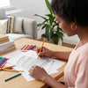 Woman coloring a detailed design with colored pencils on a table in a home setting.