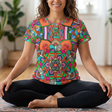 Woman sitting on a yoga mat wearing a colorful mandala-patterned shirt in a home setting.