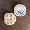 Two round floor poufs on a dark wood floor. One pouf has a white background with a repeating pattern of orange tabby cats, and the other has a white background decorated with colorful cat-themed graphics including paw prints, fish bones, and a blue swirl.