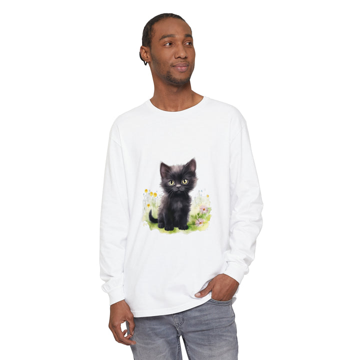 A cute black kitten sits in a vibrant flower garden on a long sleeve t-shirt