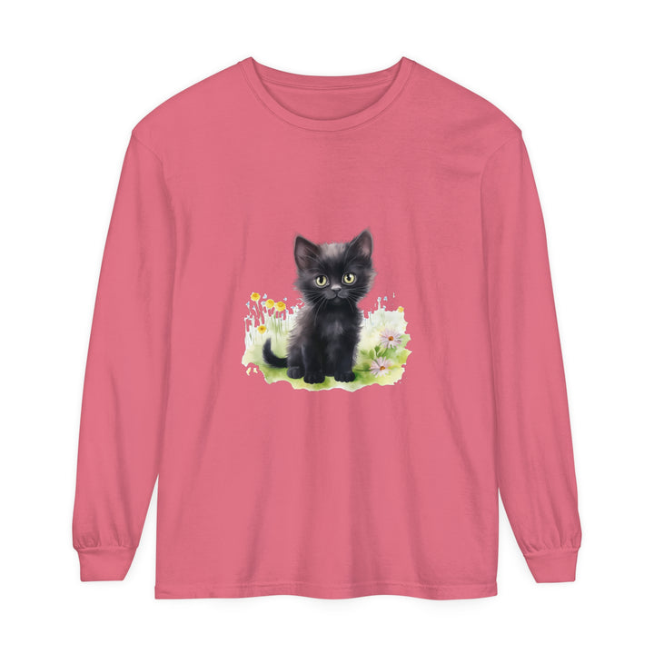 A cute black kitten sits in a vibrant flower garden on a long sleeve T-shirt