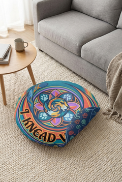 Lifestyle shot of a round floor pillow with a blue-dominant winter sacred-geometry cat design, featuring a curled cat motif, geometric rings, and vibrant colors in a cozy living room setting.