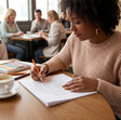 Woman coloring in a book with colored pencils at a table in a cafe.