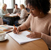 Woman coloring in a book with colored pencils at a table in a cafe.