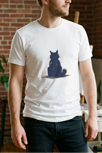 Man wearing a white t-shirt with a graphic design of a cat sitting on a moon, standing in a room with plants and art supplies.