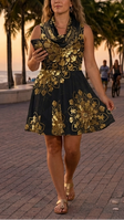 A woman walking on a tropical boardwalk at sunset, wearing a sleeveless black dress with large gold floral mandala art on classic black. Palm trees line the walkway next to the ocean, and other pedestrians are visible in the background.