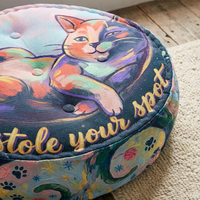 Close-up view of a round tufted floor pillow with a winter Cozy Cat design in deep navy, mint, coral, and gold highlights; lifestyle setting showing a cozy home corner with soft lighting (oil painting style).