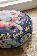 Close-up view of a round tufted floor pillow with a winter Cozy Cat design in deep navy, mint, coral, and gold highlights; lifestyle setting showing a cozy home corner with soft lighting (oil painting style).