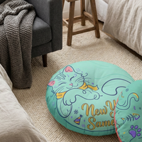 Winter New Year Cozy Cat round tufted floor pillow in bold colors: coral pink, yellow, teal, navy. Lifestyle setting showing a cozy living room with the cat design on a chair, emphasizing warm mood and line-art cat motif.