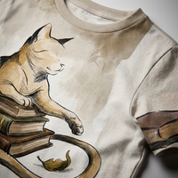 Dark Academia t-shirt with a cloaked cat illustration in muted browns and greens on a deep, earthy background. Lifestyle studio flatlay showing the cat perched over books in a scholarly, cozy setting. Close-up highlights the draped cat and book motif.