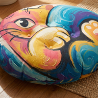 Round floor pillow featuring a curled cat in pink and yellow tones with oil-painting and simple cartoon line art; lifestyle setting showing cozy playful comfort in a living room corner