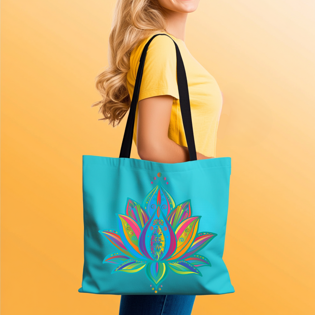A woman in a yellow shirt holds a turquoise lotus flower mandala tote bag with a colorful mandala-style lotus flower design. The bag has black shoulder straps and is shown against a warm yellow gradient background.