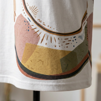 Beige t-shirt with a Cozy Crescent Cat boho line art design, shown in a lifestyle flatlay with warm neutrals and soft lighting; colors include beige, tan, and muted gold, emphasizing a calm, cozy vibe.