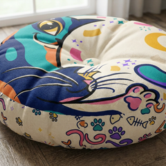 Close-up of a round tufted floor pillow with a curling crescent cat line-art in a winter palette (navy, teal, gold, pink, cream). Cozy, playful home setting for late-December, with soft fabrics and bright colors.