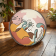 Round tufted cat floor cushion in warm boho colors with playful line-art cat design; living room lifestyle scene showing cozy, inviting atmosphere