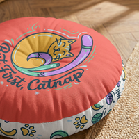 Close-up lifestyle shot of a Cozy Curl Cat Floor Pillow in warm coral (#FF6B6B) featuring a curled cat line-art design with mint, lilac, and navy accents; cozy winter cat theme in a living corner setting.