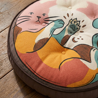 Orange-tinted round floor pillow with a whimsical boho cat line-art design, shown in a lived-in living room setting for lifestyle context.